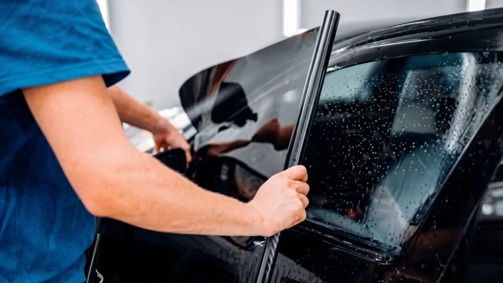Profissional instalando película automotiva no vidro lateral de um carro, respeitando as normas e a chancela do insulfilm permitido por lei em 2026.